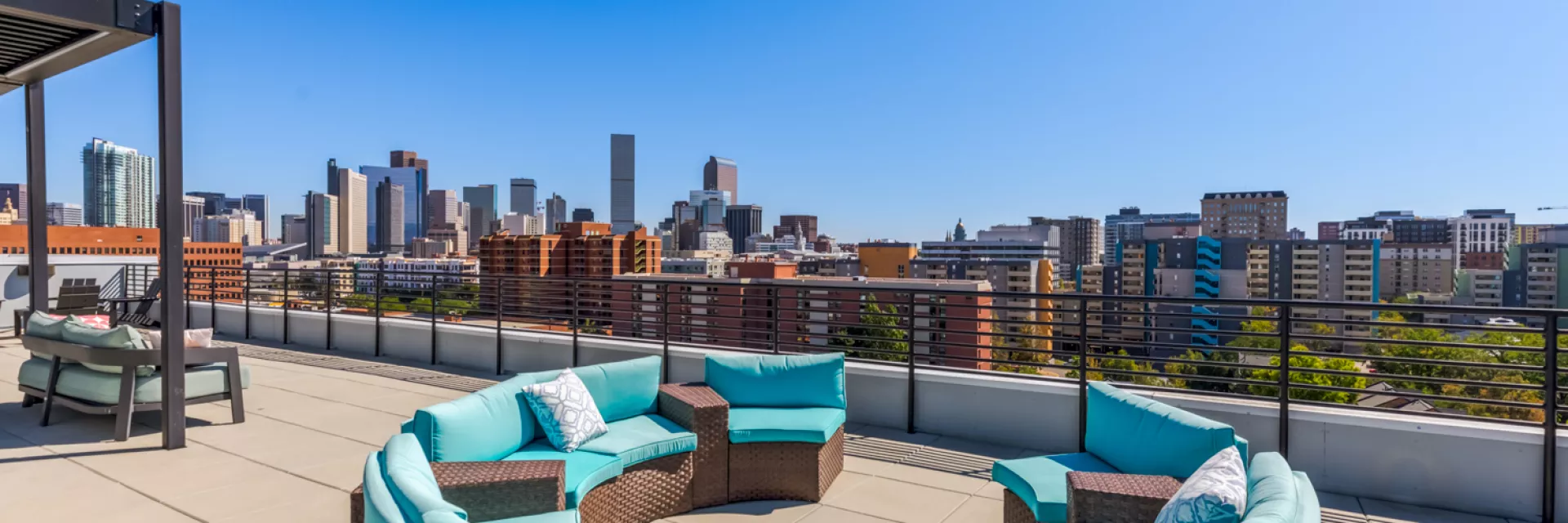 Rooftop patio with circular blue-cushioned sofa, smaller seating, and a city skyline under a clear blue sky.