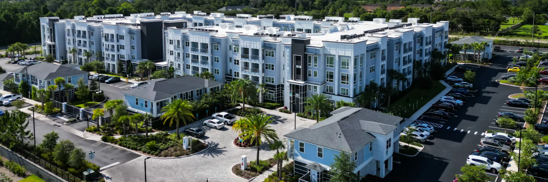 Aerial view of a large, modern apartment complex featuring several multi-story buildings, parking lots, and small accessory buildings.