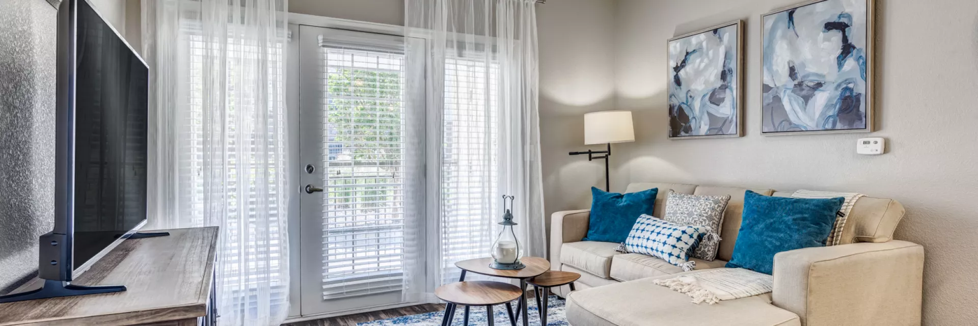 Living room with a beige sectional sofa, blue pillows, blue rug, TV, and balcony doors.