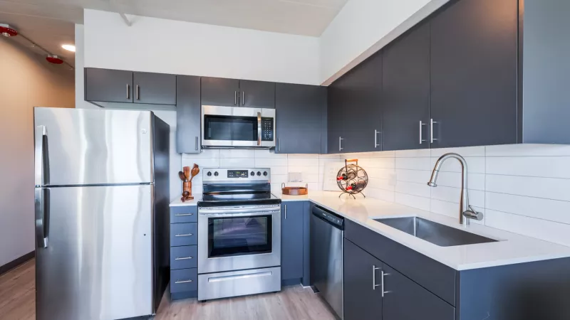 Photograph: Modern kitchen with dark grey cabinets, stainless steel appliances, white counters, and subway tile backsplash.