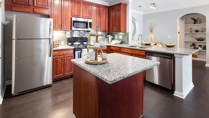 Modern kitchen with dark cherry cabinets, stainless steel appliances, light granite countertops, and island.