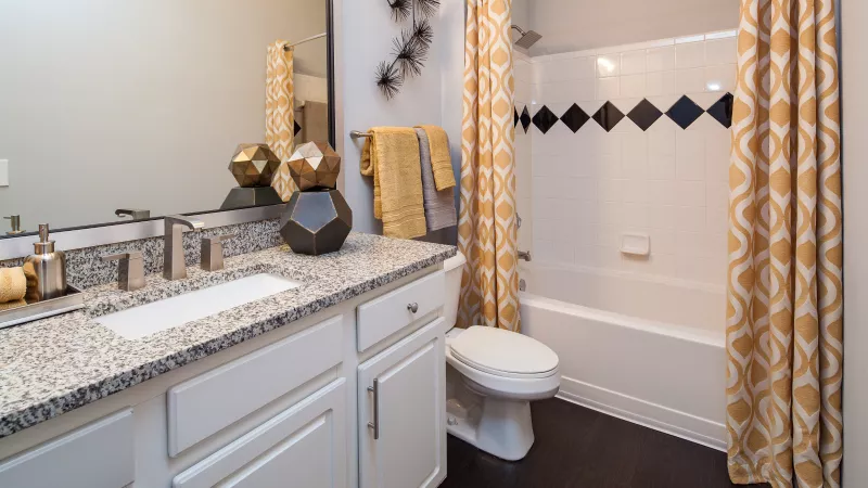 Modern bathroom with a white vanity, granite counter, toilet, and shower with a gold patterned curtain and black diamond tiles.