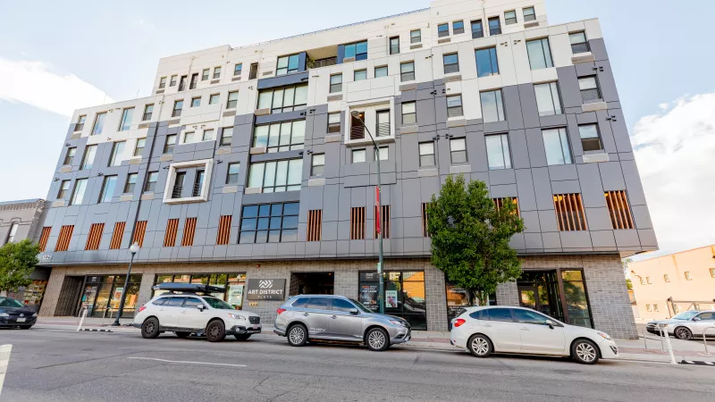 Modern multi-story building with a gray, white, and brown paneled facade. Cars are parked along the street below.