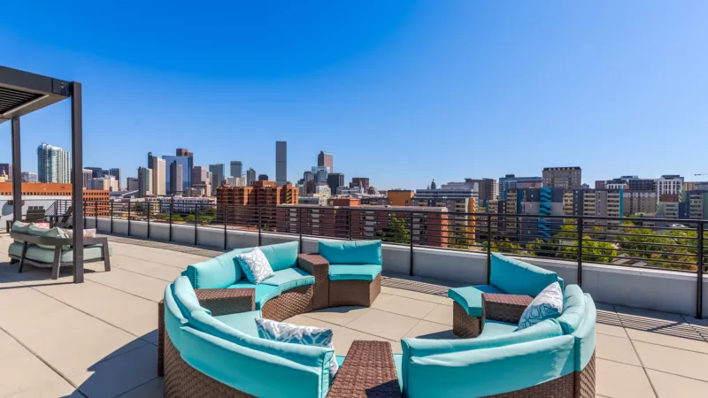 Rooftop patio with a circular teal sofa and city skyline in the background under a clear blue sky.