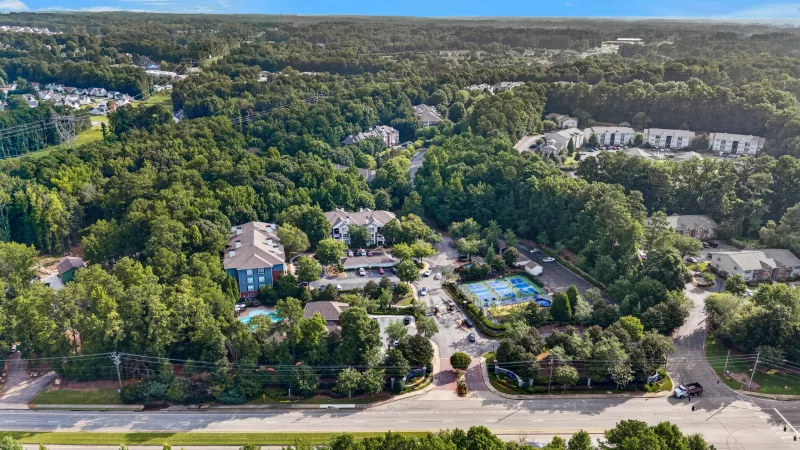 Aerial view of a green residential community with buildings, dense trees, roads, a pool, and tennis courts.