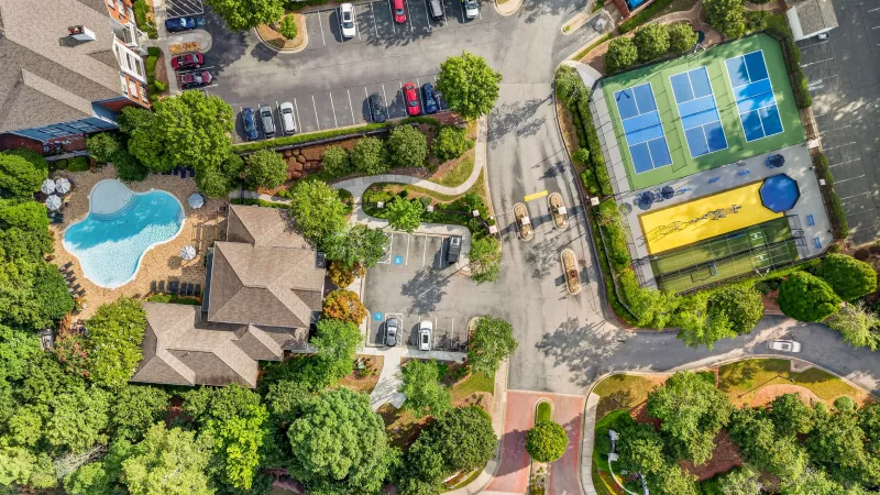 Aerial photograph of a residential complex with a light blue pool, brown buildings, blue tennis courts, and a yellow bocce court.