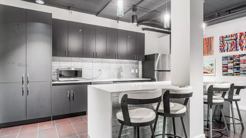 Modern office kitchen with dark gray cabinets, white island, two stools, and colorful abstract art.