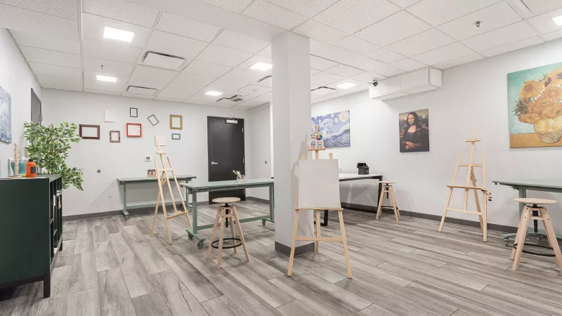 Spacious art studio with easels, tables, and art supplies. Famous painting reproductions adorn the walls, ready for creativity.