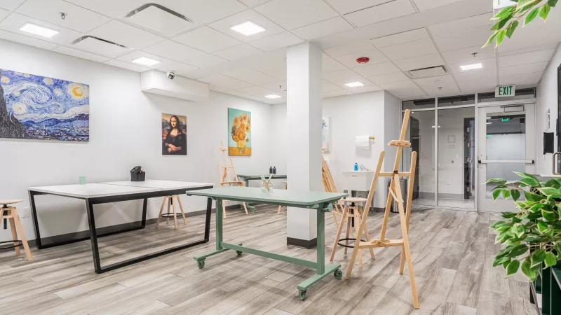 Bright art studio with tables, easels, and colorful paintings on white walls.