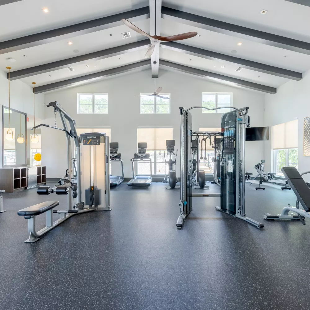 Spacious, well-lit gym with high ceilings, exposed beams, and various exercise equipment including treadmills and weights.