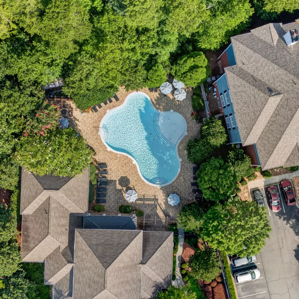 Aerial view of an apartment complex with a large, light blue swimming pool surrounded by buildings and green trees.