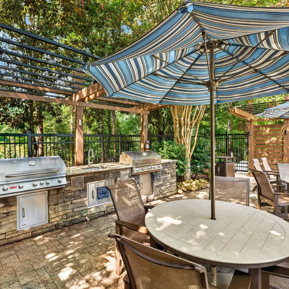Outdoor patio with two built-in grills, stone countertops, and dining tables with blue striped umbrellas.