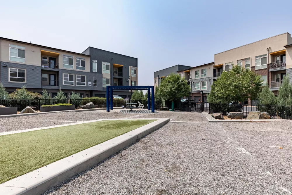 Gravel courtyard with modern apartment buildings, a blue pergola, and artificial turf.